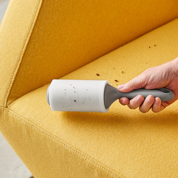 A hand using a 3M Scotch-Brite lint roller on a yellow couch.