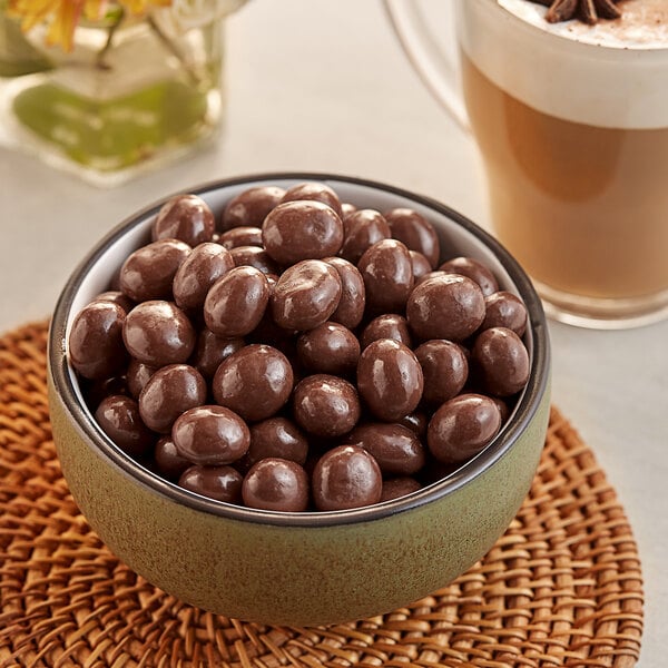 A bowl of Capora milk chocolate covered espresso beans next to a cup of coffee.