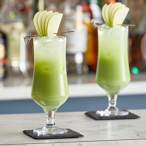 Two glasses of green apple drinks with apple slices on top on a table.