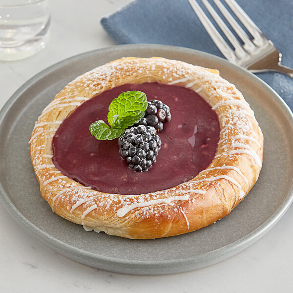 A pastry with Perfect Puree blackberry puree and berries on top on a plate with a fork.