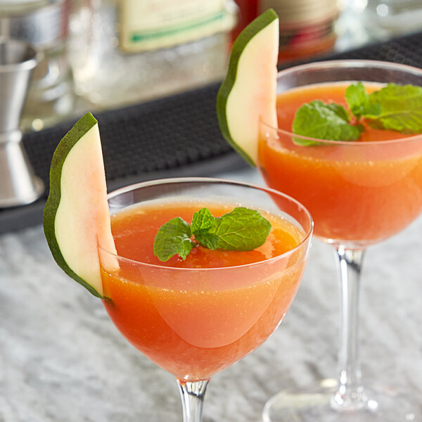 Two glasses of orange drink with a slice of fruit and mint on a marble bar.