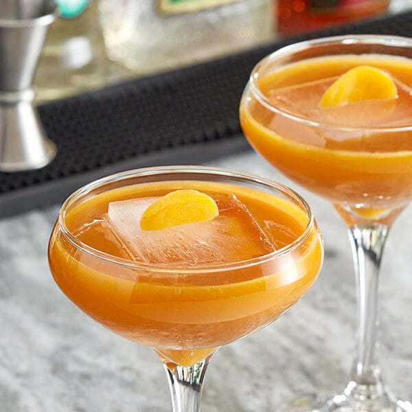 Two glasses of apricot liquid with ice and orange slices on a bar table.