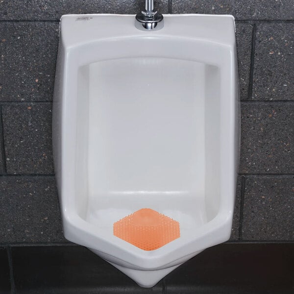 A white urinal with an orange scented urinal screen placed at the bottom.