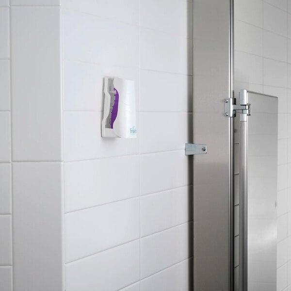 A wall-mounted passive air freshener refill in a white plastic holder on a tiled restroom wall.