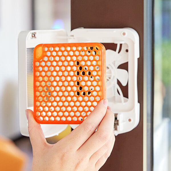 A hand holding an orange plastic grid over a white fan.