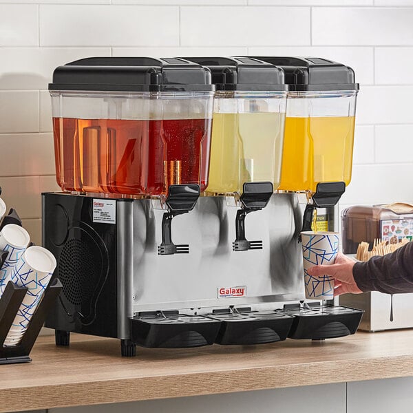 A man pouring brown liquid into a Galaxy refrigerated beverage dispenser.