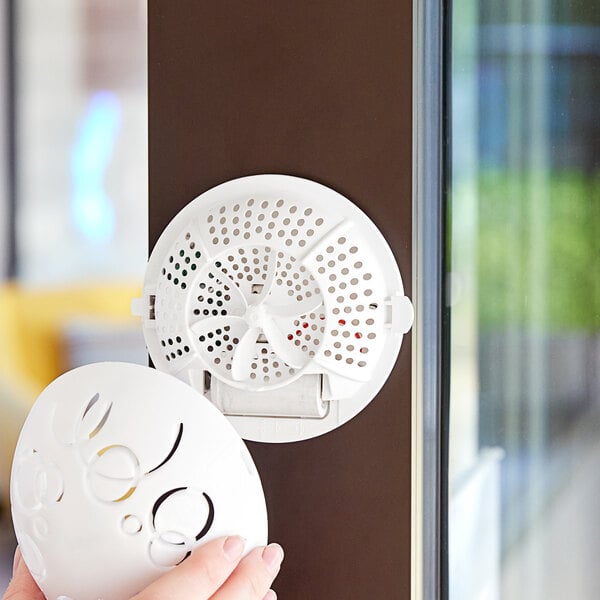 A hand holding a white Fresh Products Easy Fresh air freshener in front of a door.