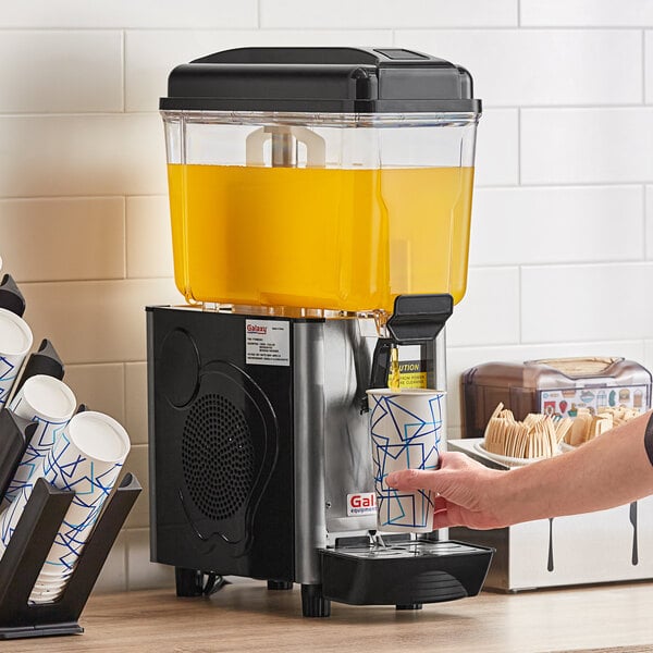 A person pouring orange juice from a Galaxy Single Bowl Refrigerated Beverage Dispenser into a cup.