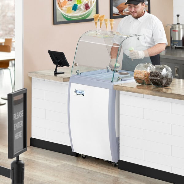 A man in a white uniform and cap using a white and grey Avantco ice cream dipping cabinet.