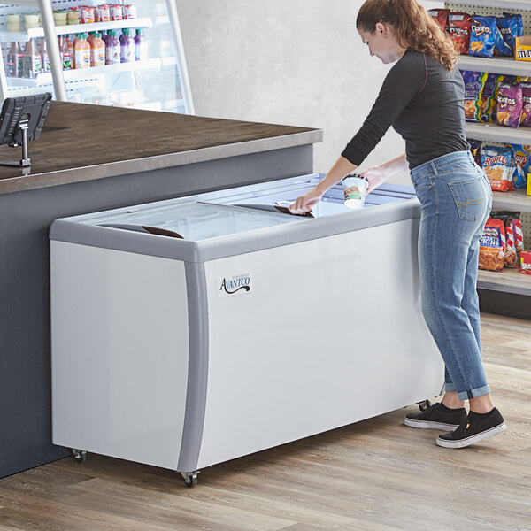 An Avantco flat top display ice cream freezer with a woman holding a cup opening the lid.