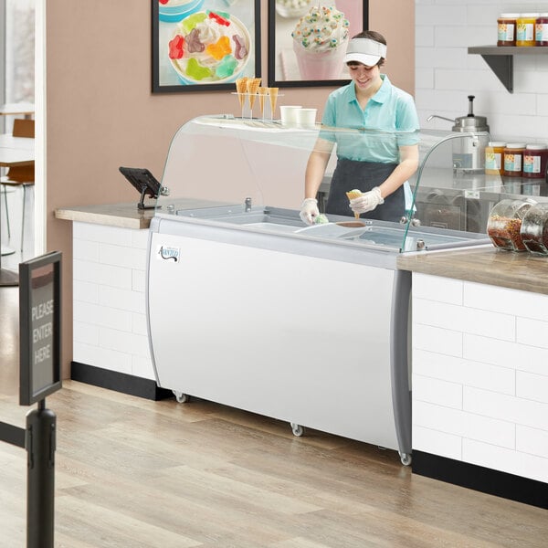 A woman in a white cap and gloves serving ice cream from an Avantco ice cream dipping cabinet.