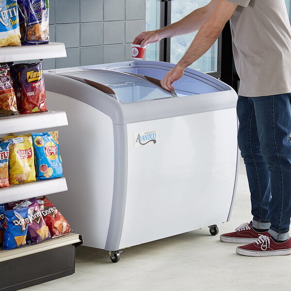 A man opening an Avantco curved glass top display freezer in a convenience store.