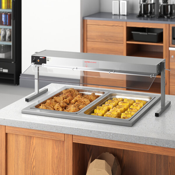 A counter with a ServIt sneeze guard over a tray of food including chicken and corn.