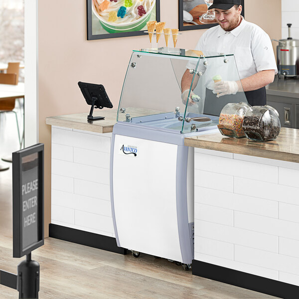 A man in a black hat holding a glass of ice cream served from an Avantco ice cream dipping cabinet.