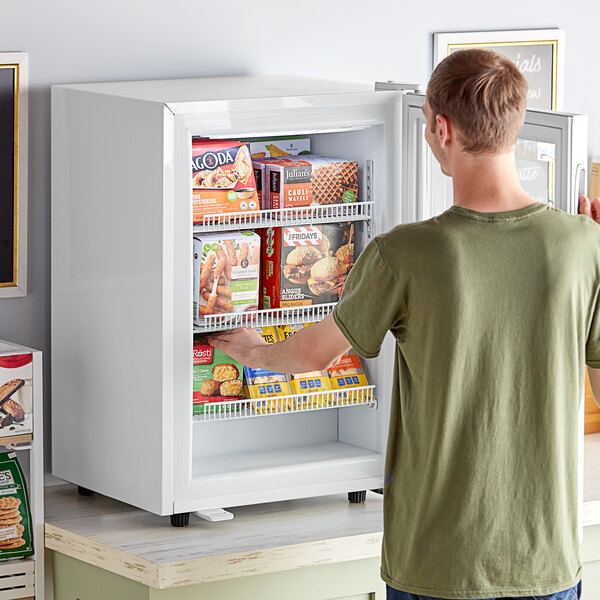 A man opening the swing door on a white Avantco countertop display freezer.