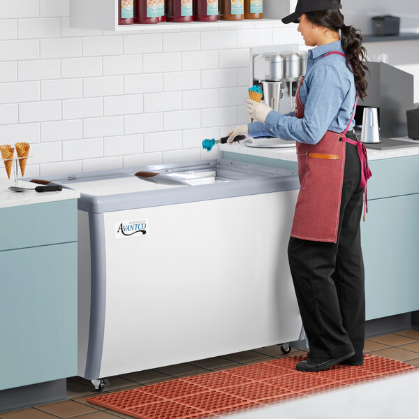 An aproned woman using an Avantco gelato dipping cabinet with pans.