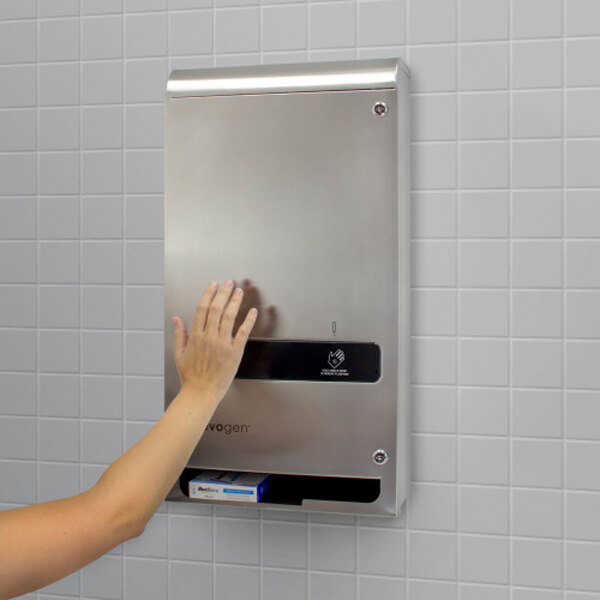 A stainless steel, surface-mounted, no-touch sanitary napkin and tampon dispenser installed on a tiled wall.