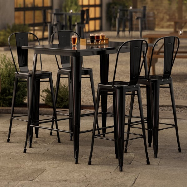 A Lancaster Table & Seating black bar height table with 4 black chairs outside on a patio.