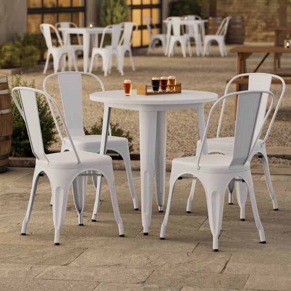 A Lancaster Table & Seating pearl white table with four chairs outside on a stone patio.