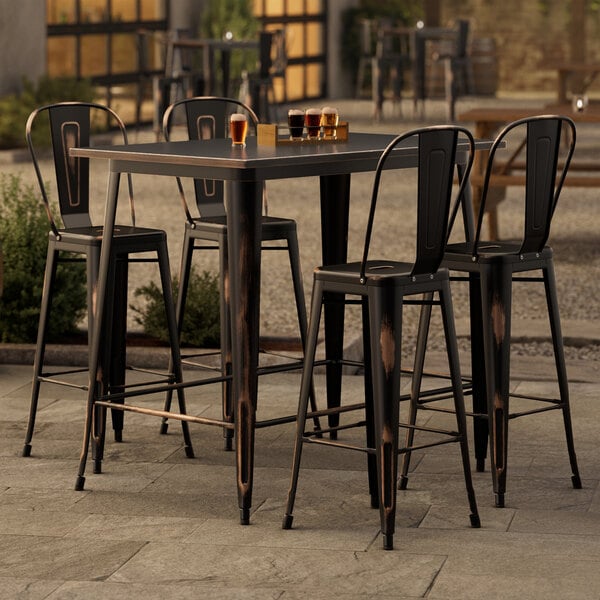 A Lancaster Table & Seating distressed copper bar table with four chairs on an outdoor patio.