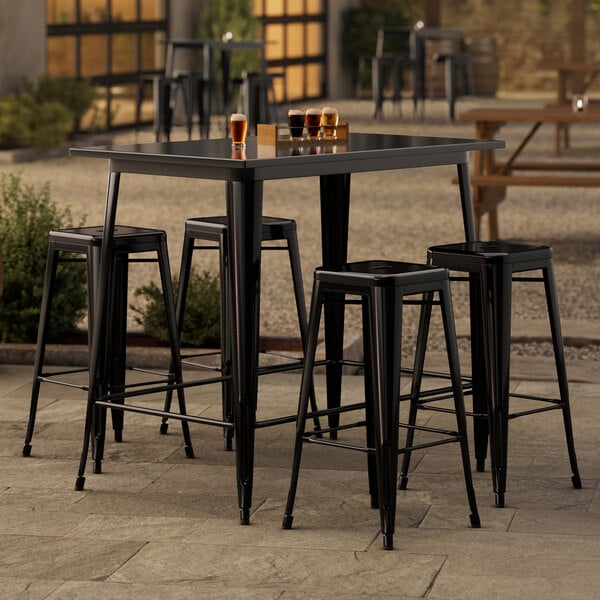 A Lancaster Table & Seating black bar table with four backless barstools on a patio.