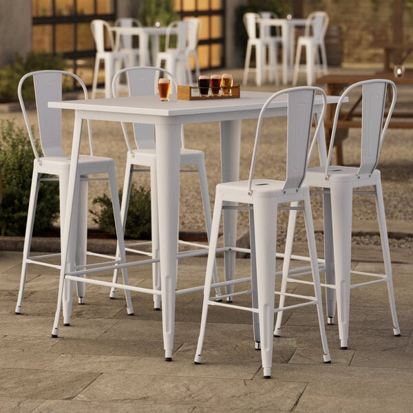 A Lancaster Table & Seating pearl white bar height table with four chairs on an outdoor patio.