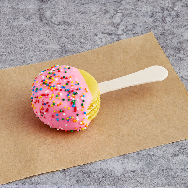 A Coco Bakery Meyer lemon macaron on a stick with white frosting and sprinkles.
