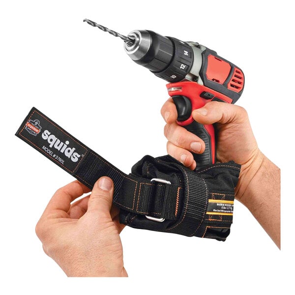 A hand holding a black fabric strap attached to a drill.