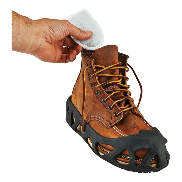 A hand using a white adhesive pad to attach an Ergodyne N-Ferno air-activated toe warmer to a brown boot.