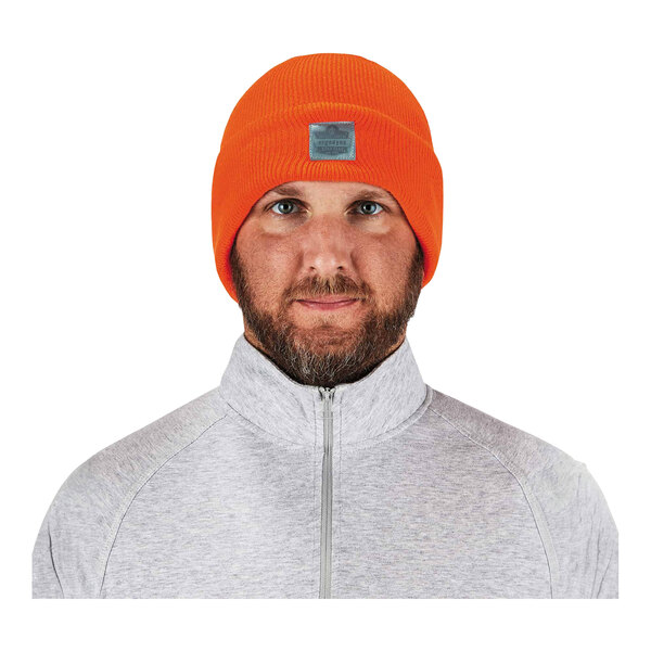 A man wearing a high visibility orange Ergodyne winter hat with a logo on it.