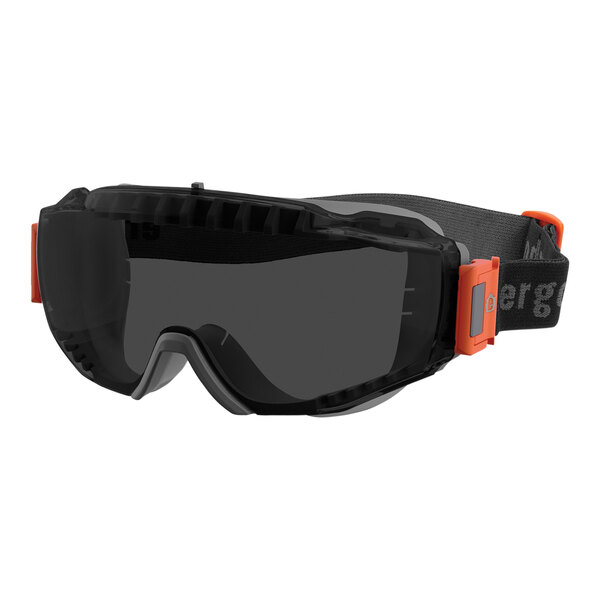 A close-up of a black and orange Ergodyne Skullerz safety goggles with a smoke lens.