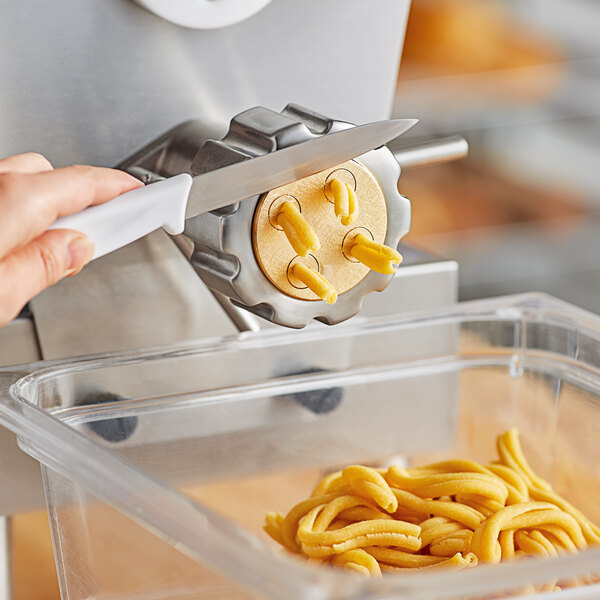 A hand using a knife to cut pasta dough on a counter.
