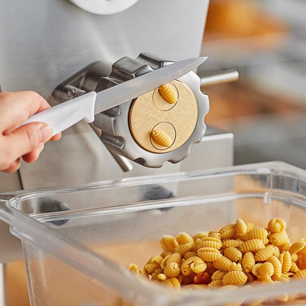 A hand cutting gnocchi pasta with a knife over a container.