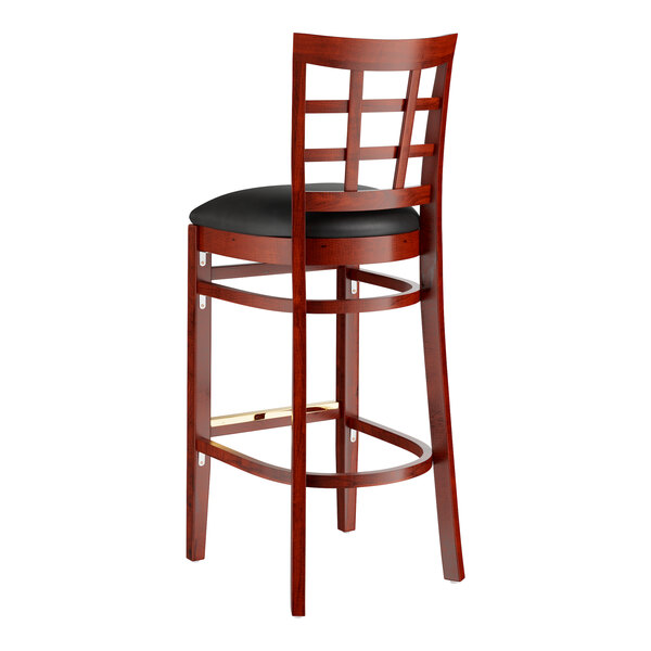 A Lancaster Table & Seating mahogany wood bar stool with black vinyl cushion.