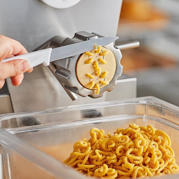 A hand using a knife to cut noodles on a counter.