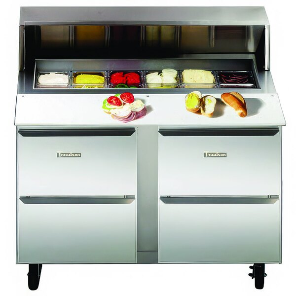 A Traulsen refrigerated sandwich prep table with a sandwich, tomatoes, onions, and green and red objects on the counter.