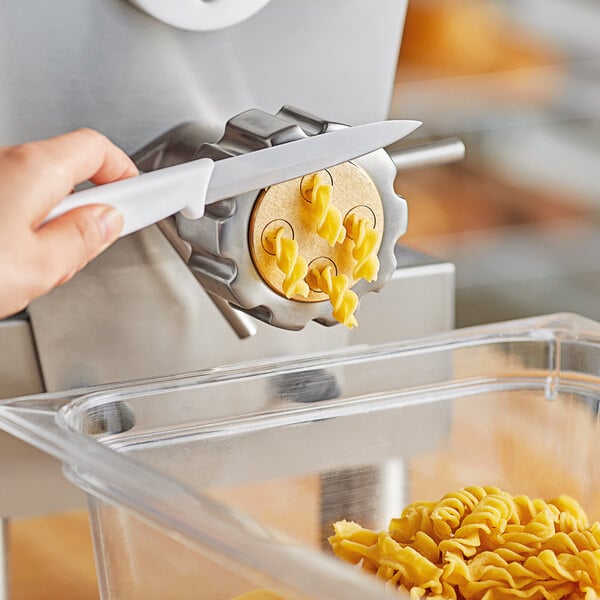 A hand using a knife to cut pasta in a pasta machine.