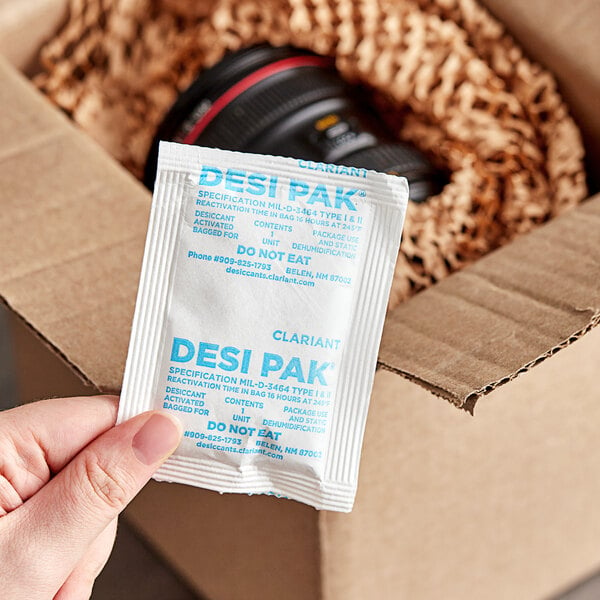 A person holding a box of Clariant Desi Pak desiccant packets.