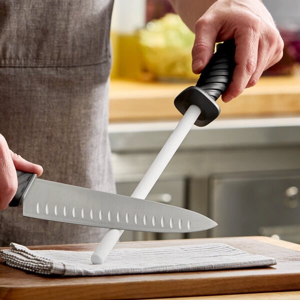 A 10-inch round ceramic sharpening rod with a black TPR grip handle being used to sharpen a kitchen knife.