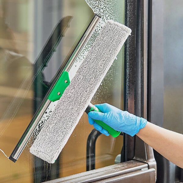 A person wearing blue gloves using a Unger VisaVersa Pro squeegee to clean a window.