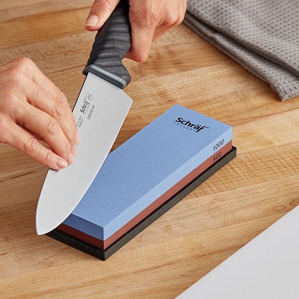 A hand holding a Schraf combination sharpening stone and a knife.
