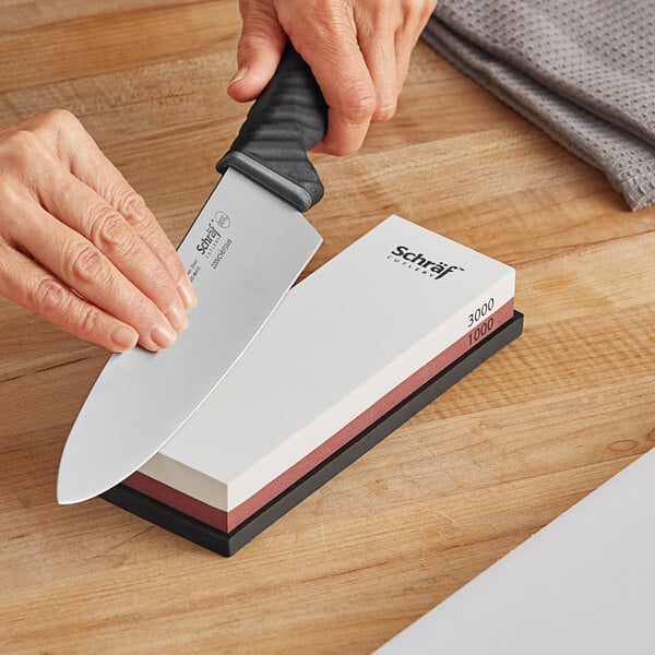 A person's hands using a Schraf combination sharpening stone to sharpen a knife.