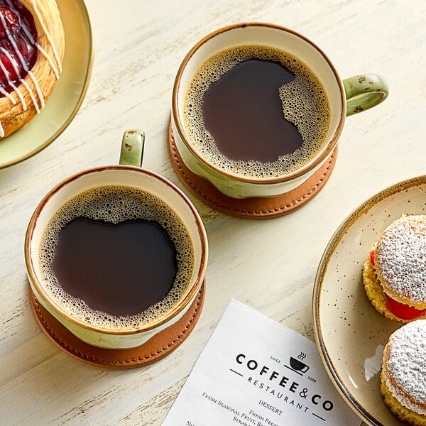 A table with coffee cups and pastries on plates, a sandwich on a plate, and a cup of coffee on a coaster.