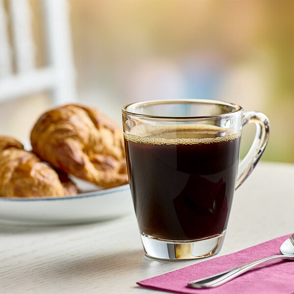 A glass cup of Green Mountain Coffee Roasters Dark Magic coffee on a table with croissants.