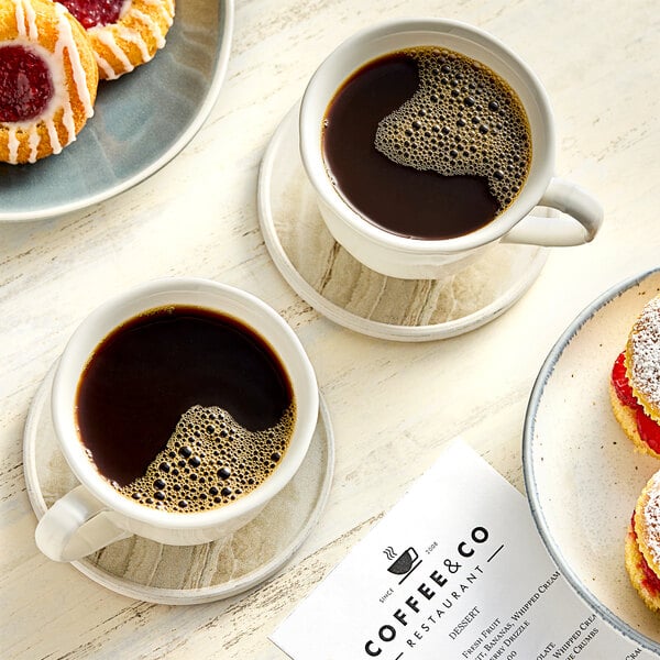 A group of coffee cups and pastries on a table with a white plate.