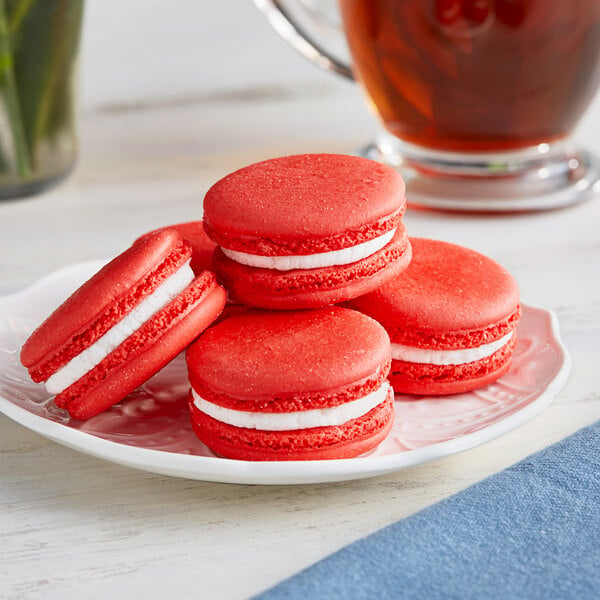 A white plate with a stack of red and white Coco Bakery red velvet macarons.