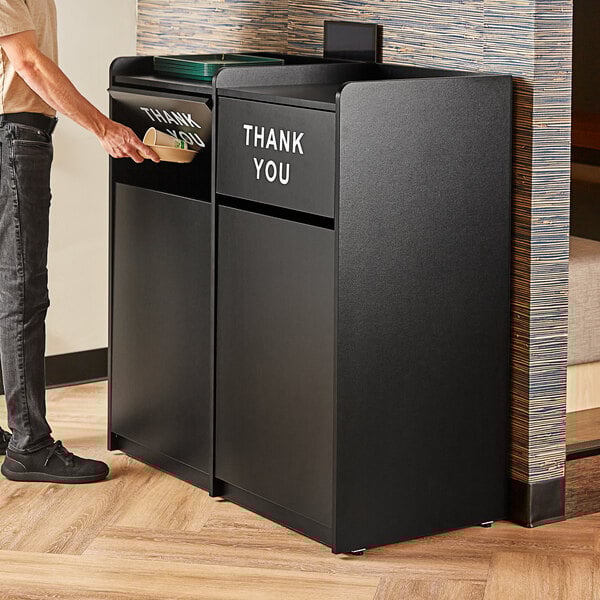 A man standing next to a black rectangular Lancaster Table & Seating waste receptacle with "THANK YOU" in white on the doors.