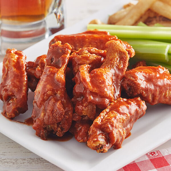 A plate of chicken wings and fries with celery sticks next to a bowl of Tapatio Hot Sauce.