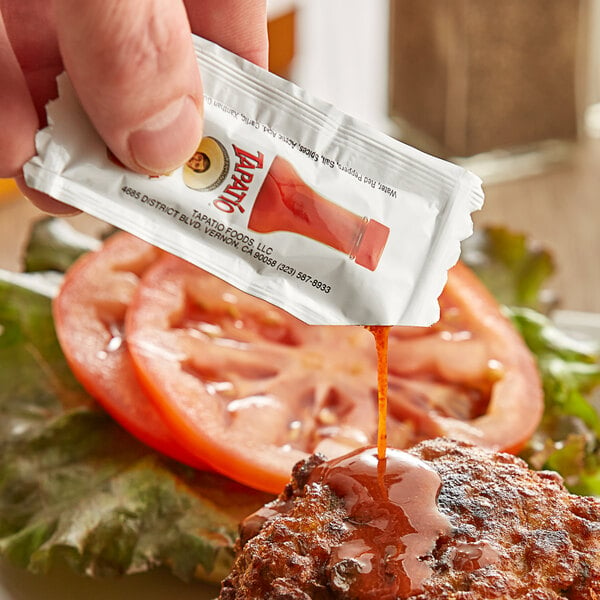 A person holding a Tapatio hot sauce packet over food.