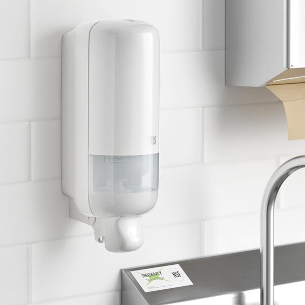 A Tork Elevation white manual foam hand soap dispenser on a wall.